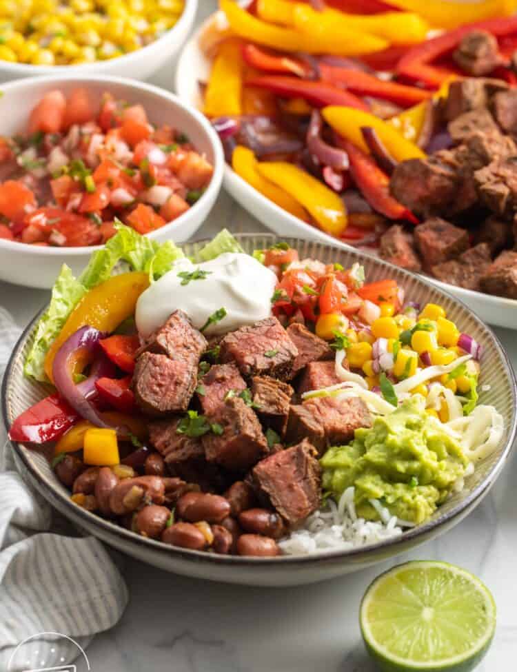 a homemade chipotle steak burrito bowl topped with sour cream, guacamole, corn, tomatoes, and cheese.