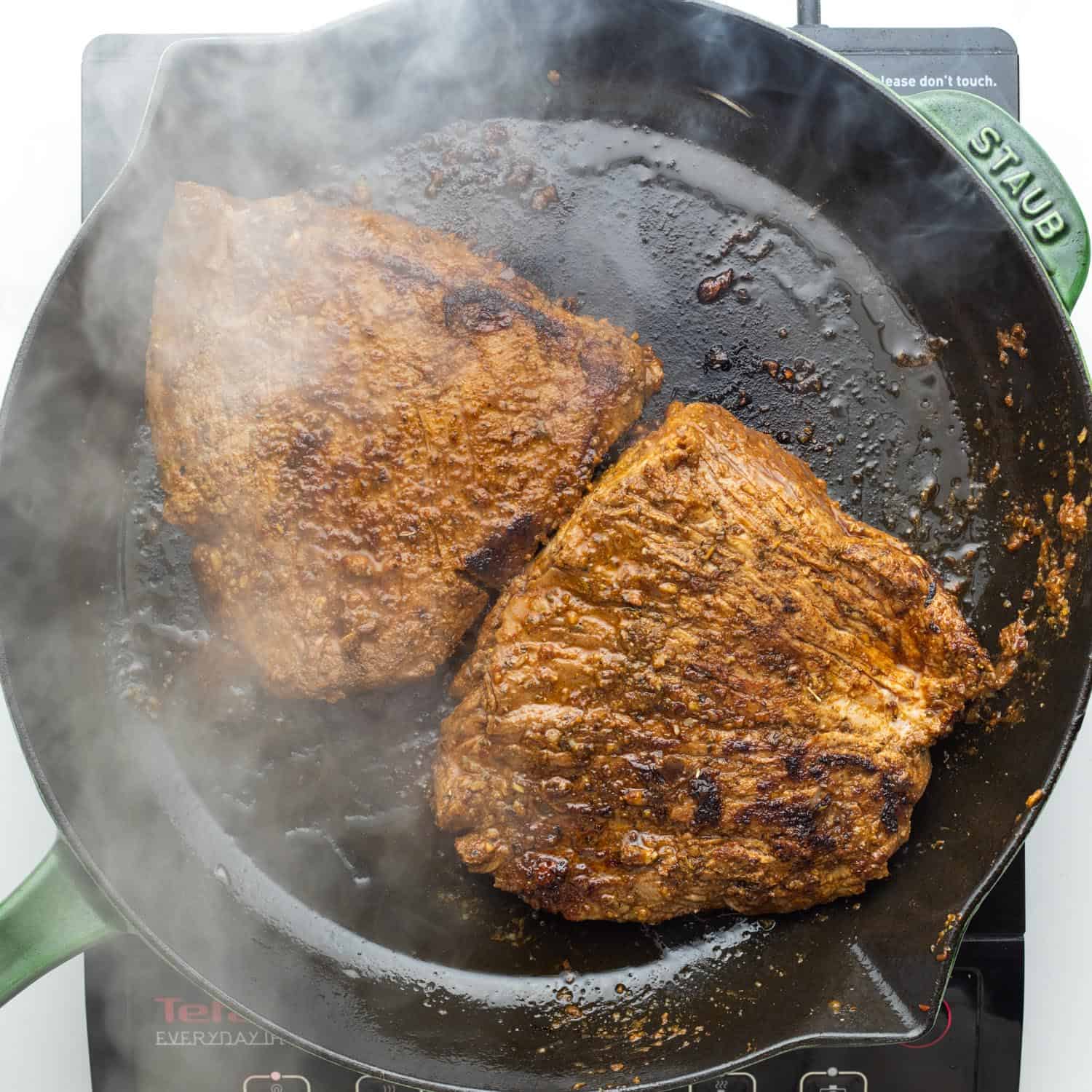 two pieces of flank steak seared in a hot cast iron skillet.