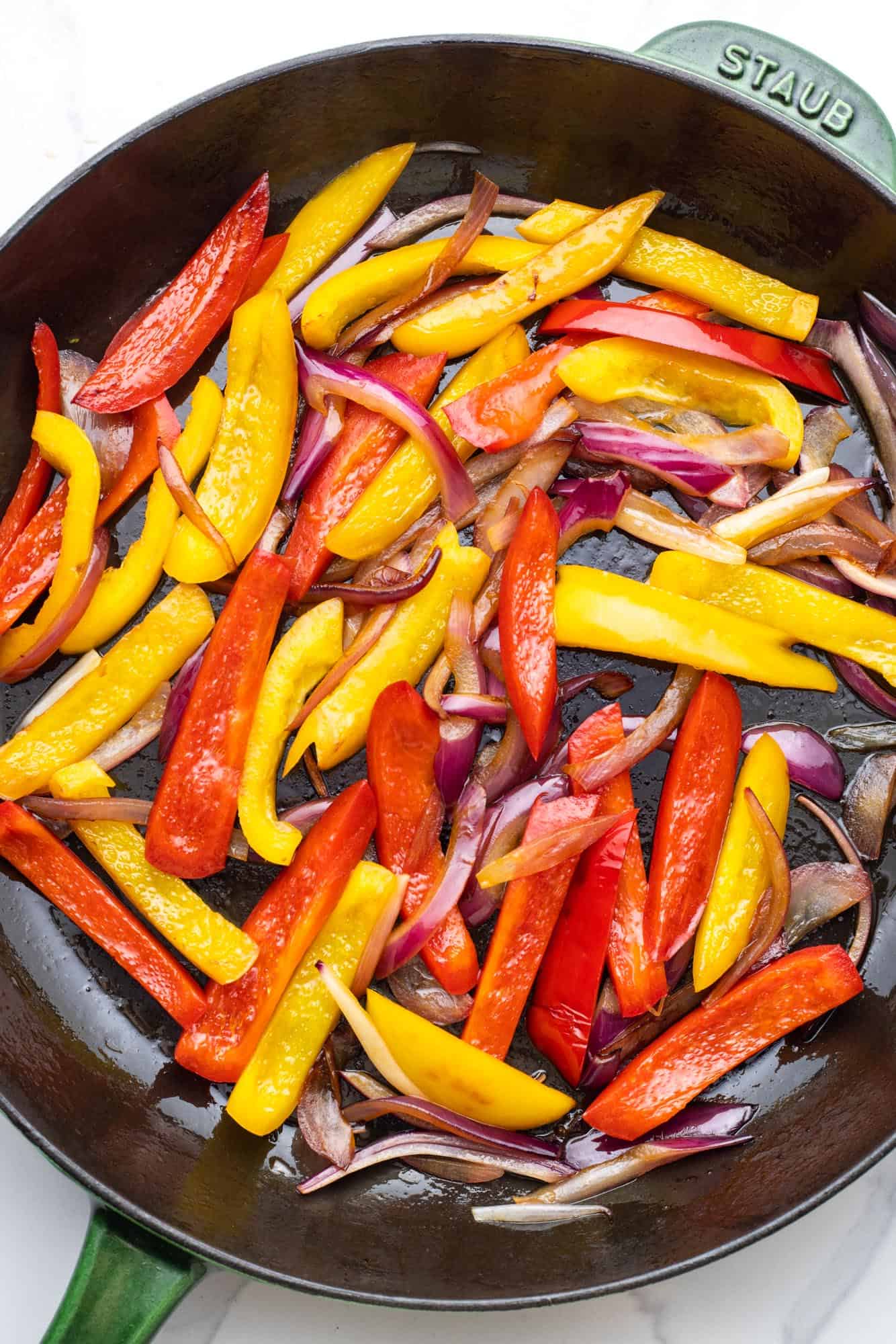 sliced onion and bell peppers cooking in a cast iron skillet.