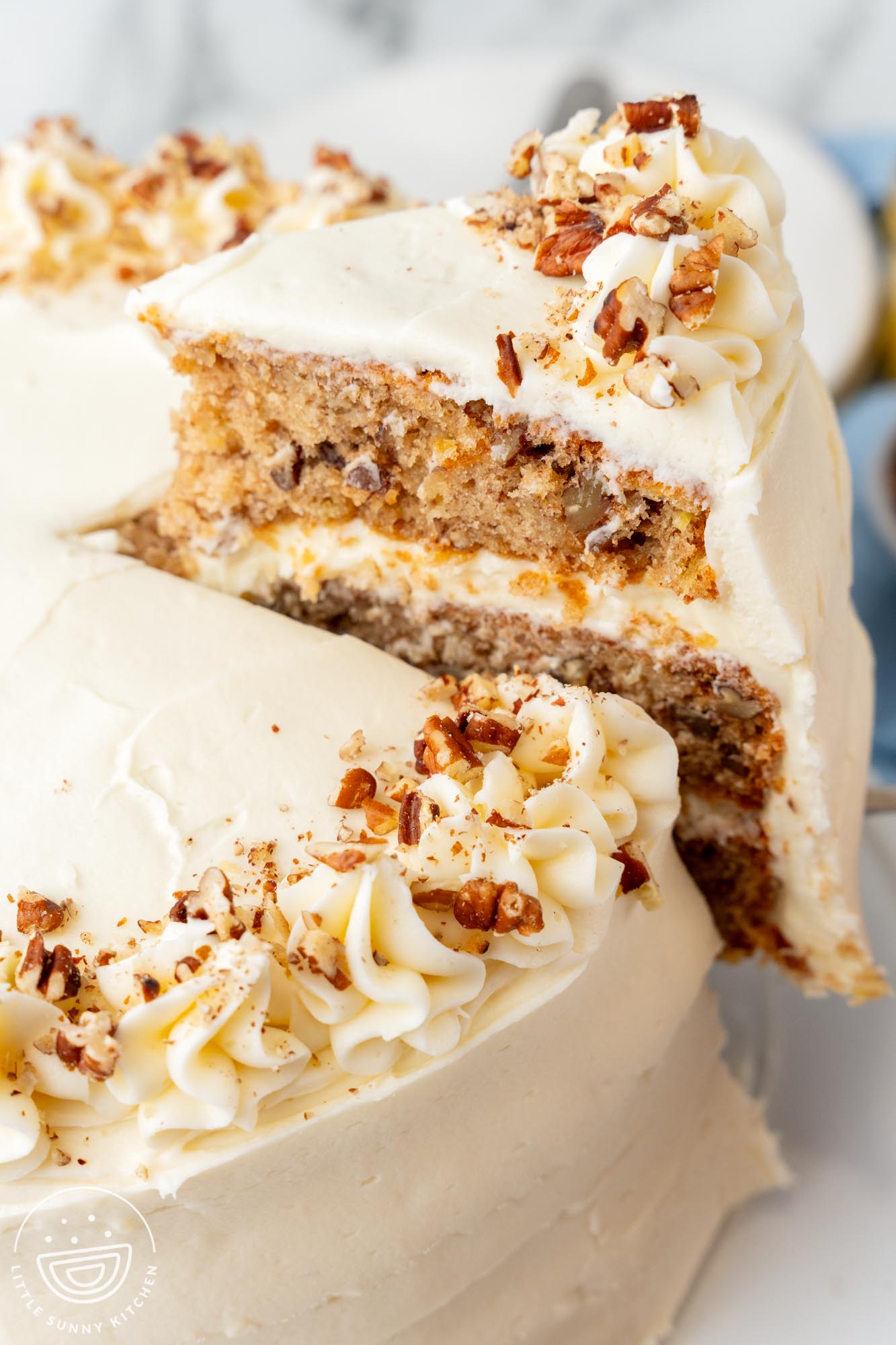 a slice of hummingbird cake with cream cheese frosting being lifted away from the whole cake.