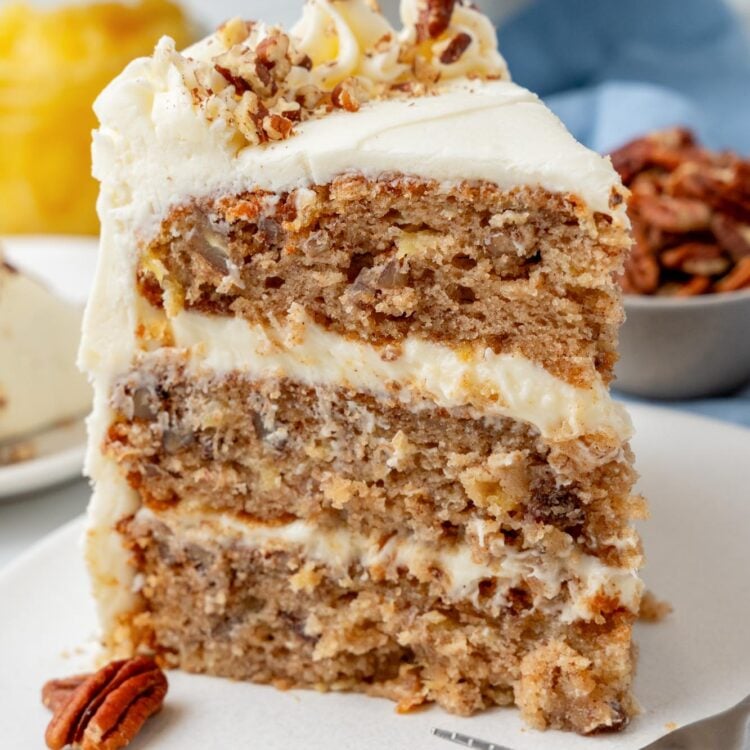 a three layer slice of hummingbird cake with pineapple and pecans on a white dessert plate.