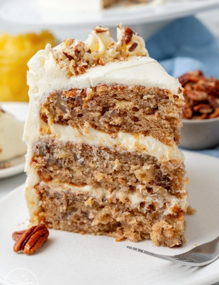 a three layer slice of hummingbird cake with pineapple and pecans on a white dessert plate.