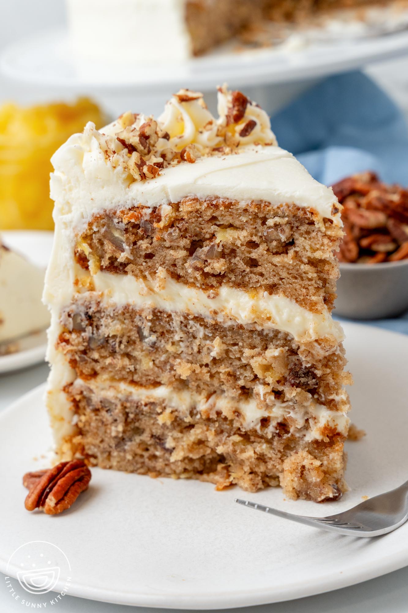 a three layer slice of hummingbird cake with pineapple and pecans on a white dessert plate.