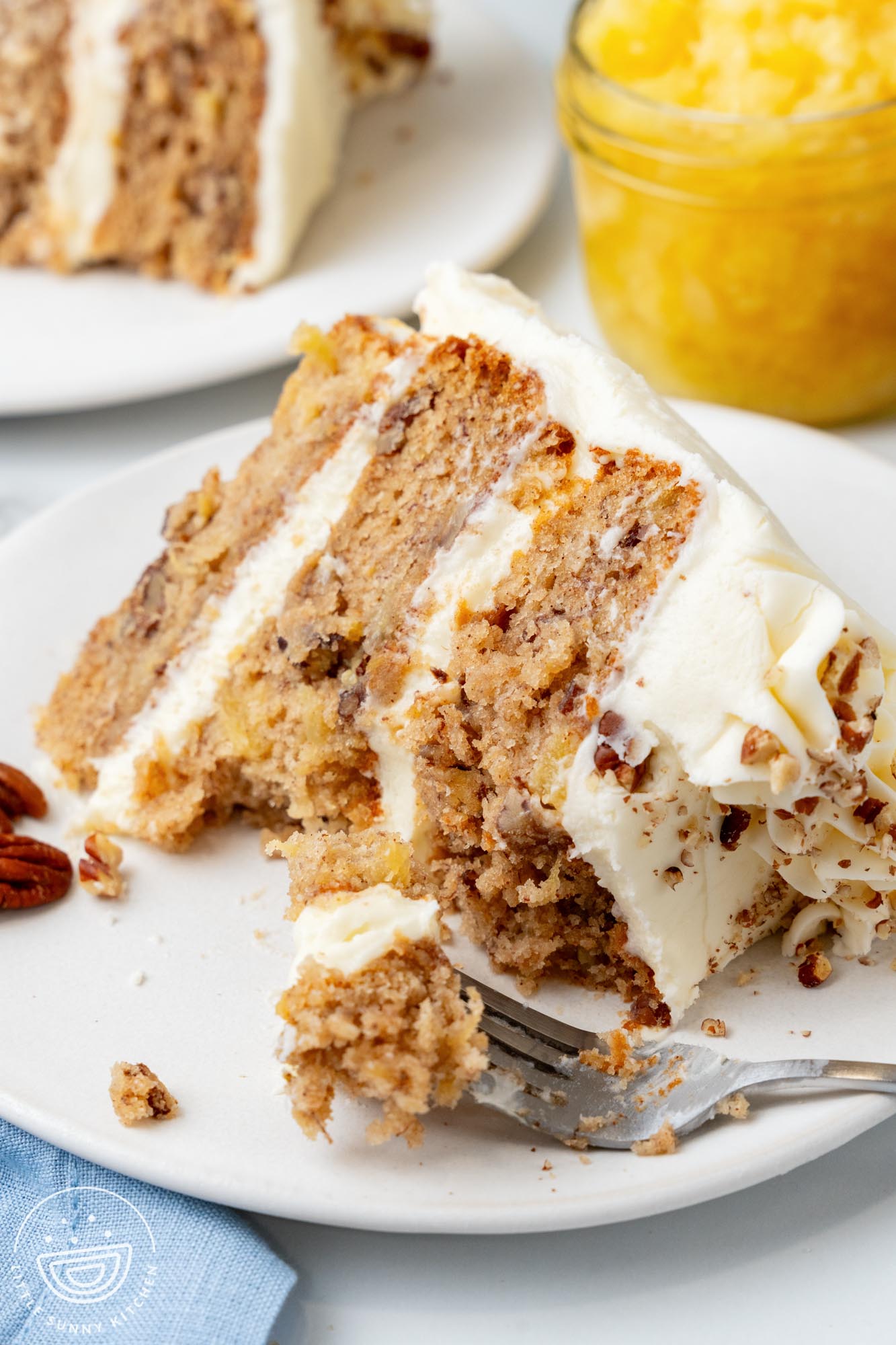 a slice of hummingbird cake on a white plate, a fork is holding a bite.