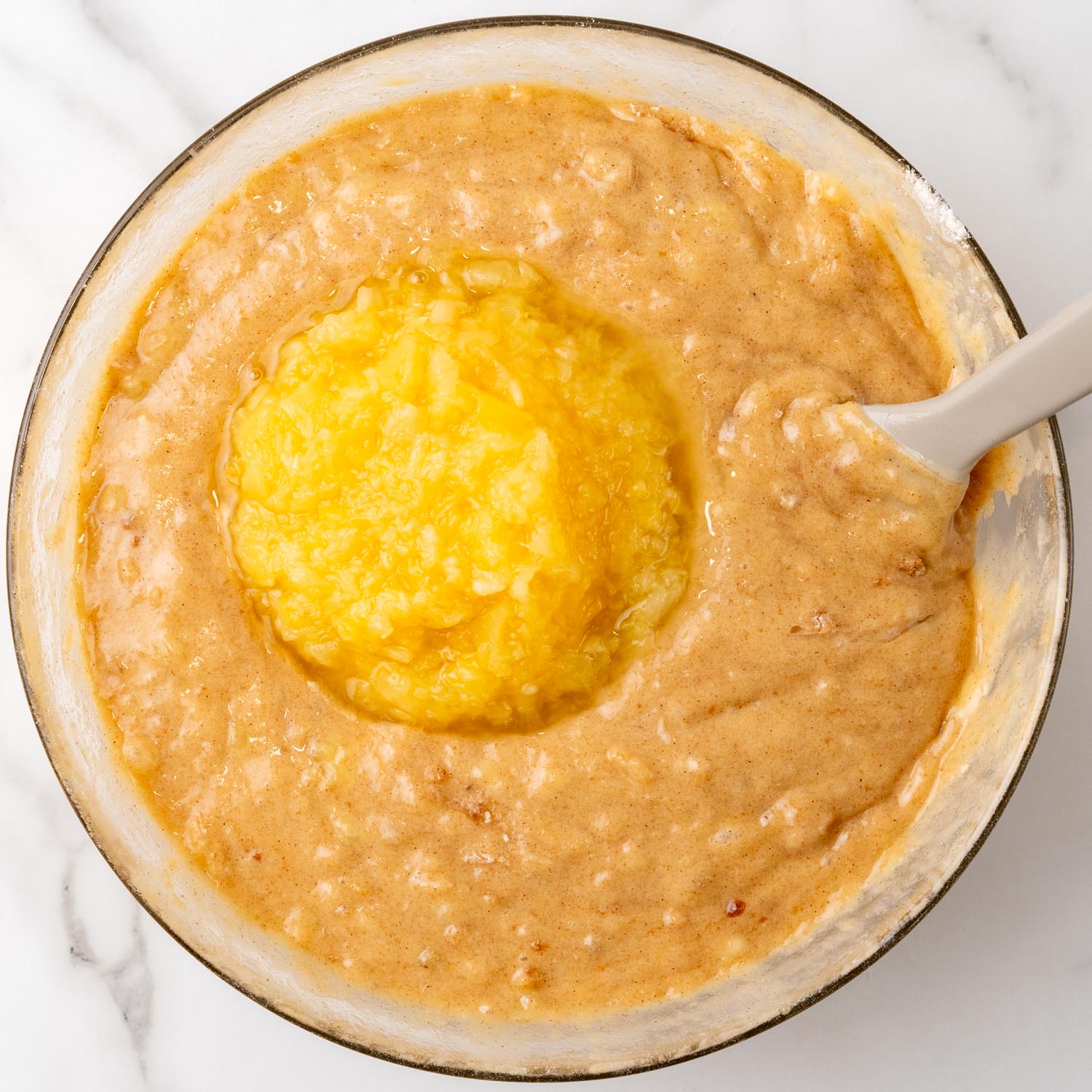 crushed pineapple added to hummingbird cake batter in a glass bowl.