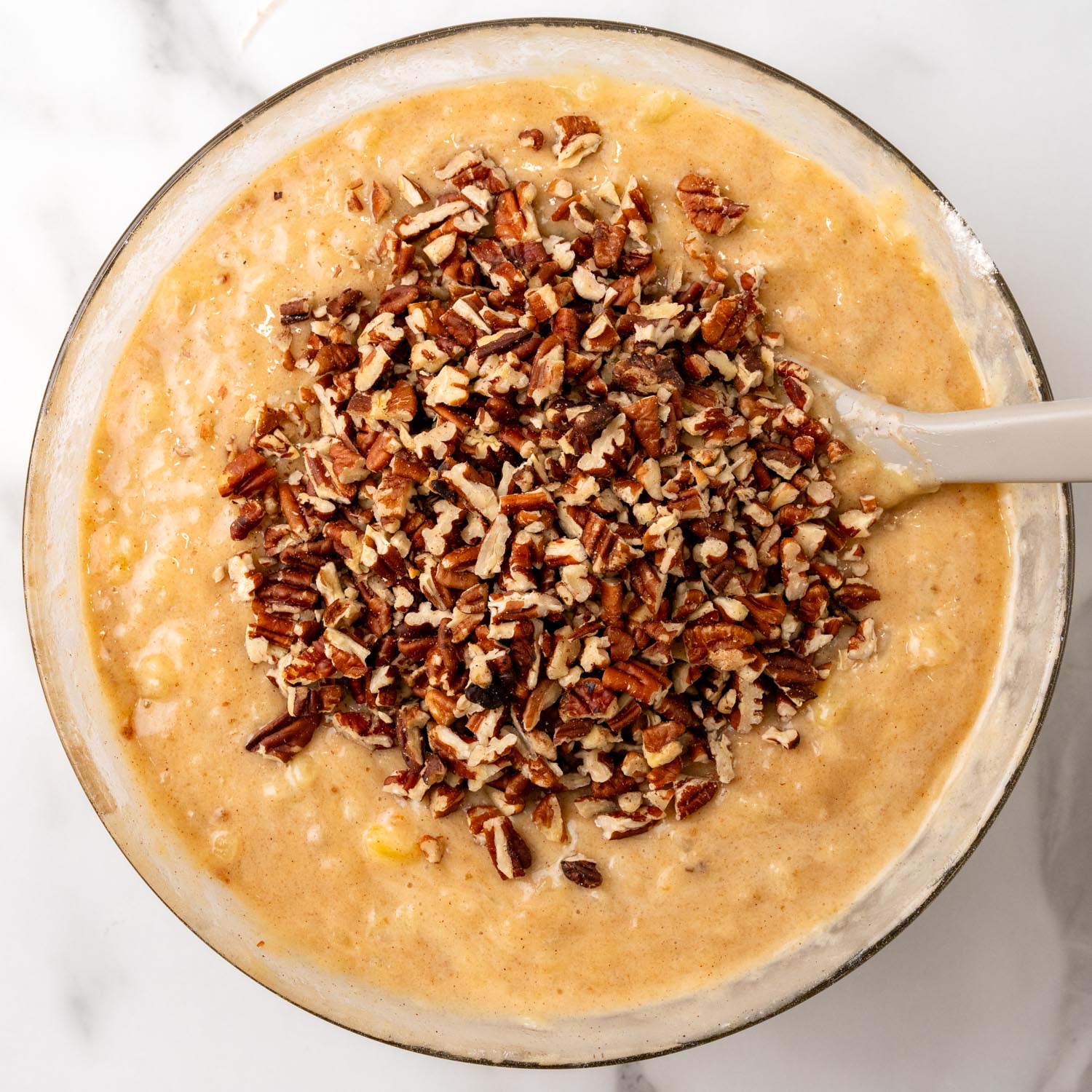 chopped pecans added to hummingbird cake batter in a glass bowl.