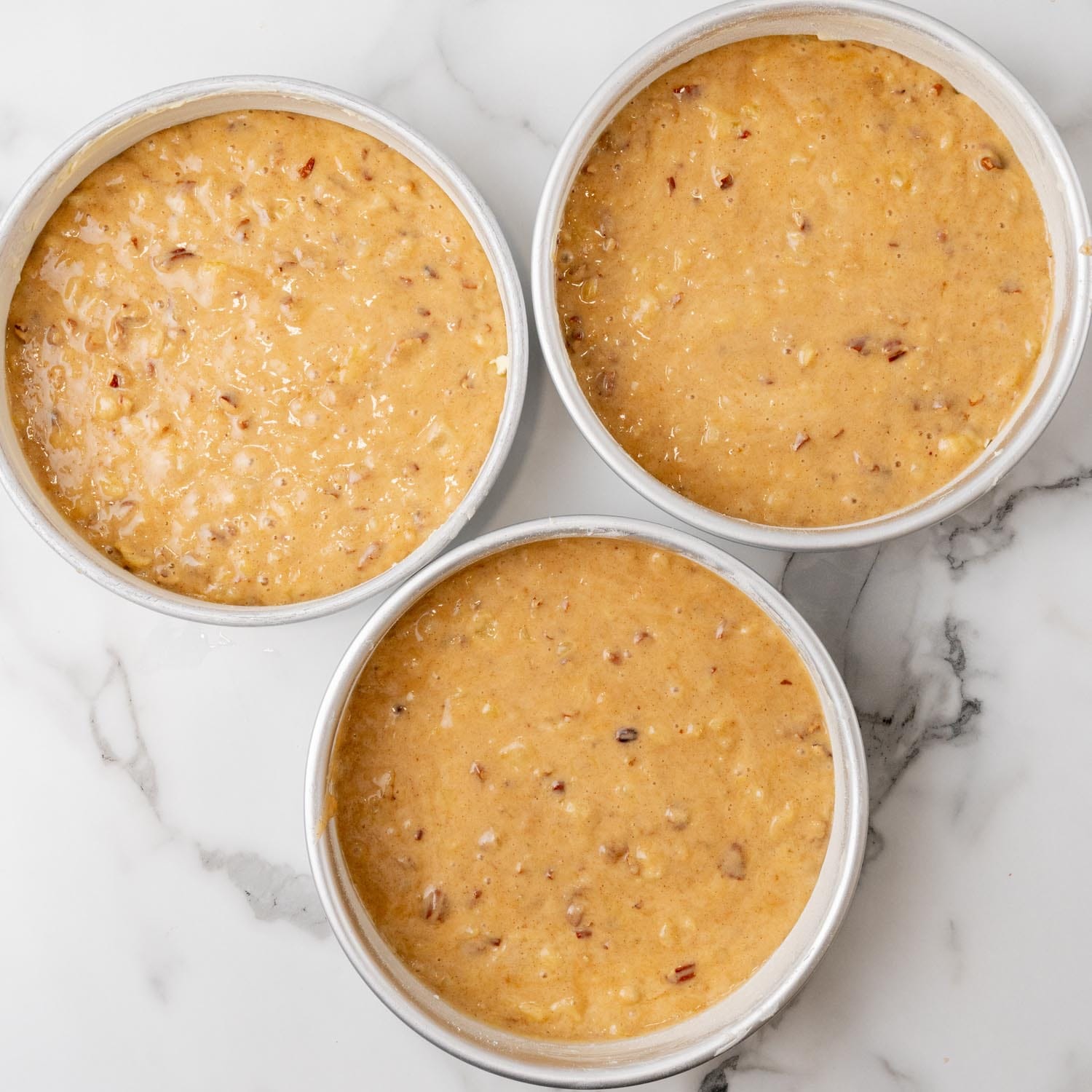 batter for hummingbird cake divided into three prepped metal pans.