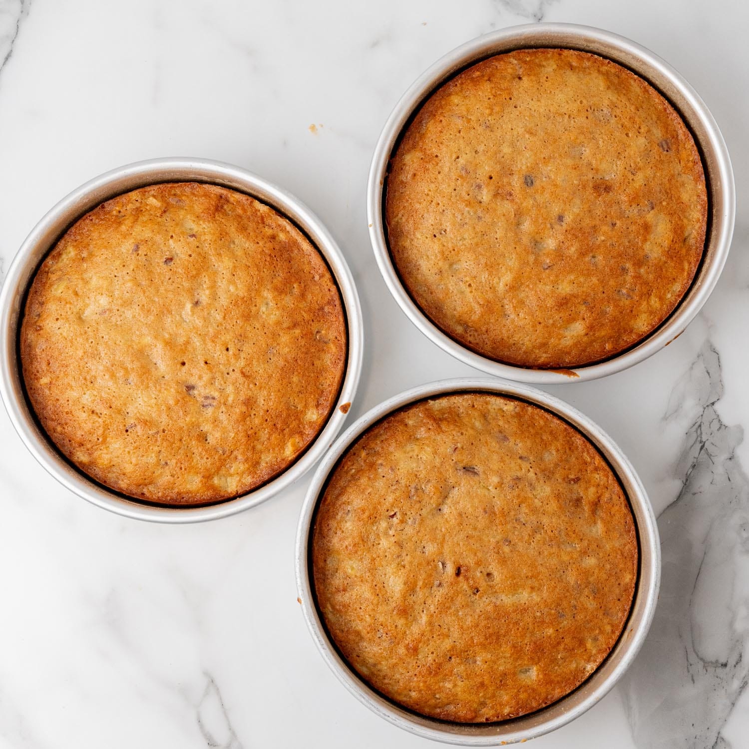 baked hummingbird cake layers in round cake pans, on a marble counter