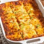 a white ceramic pan of lasagna, cut into squares, garnished with fresh parsley.