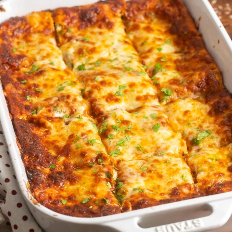 a white ceramic pan of lasagna, cut into squares, garnished with fresh parsley.