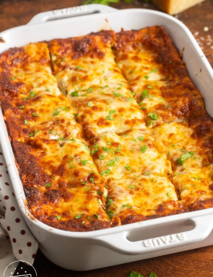 a white ceramic pan of lasagna, cut into squares, garnished with fresh parsley.