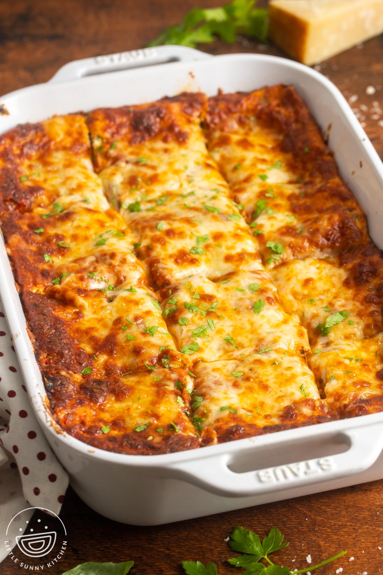 a white ceramic pan of lasagna, cut into squares, garnished with fresh parsley.