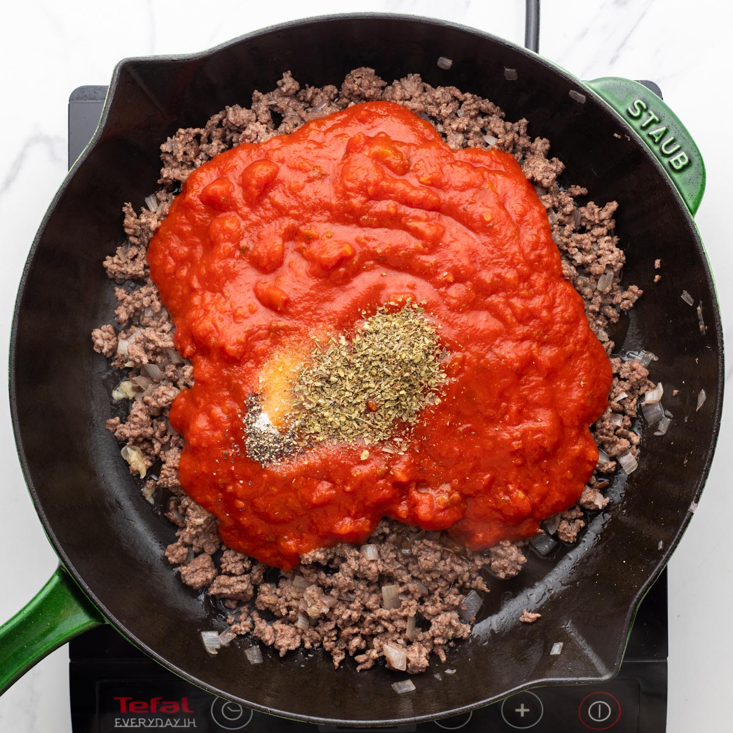 tomato sauce and seasonings added to ground beef in a cast iron skillet.