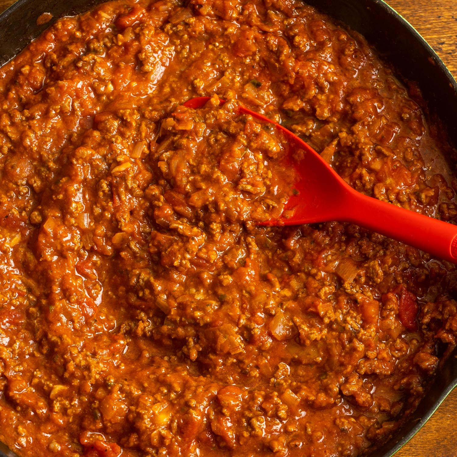 meat sauce for lasagna in a skillet, stirred with a red spoon.