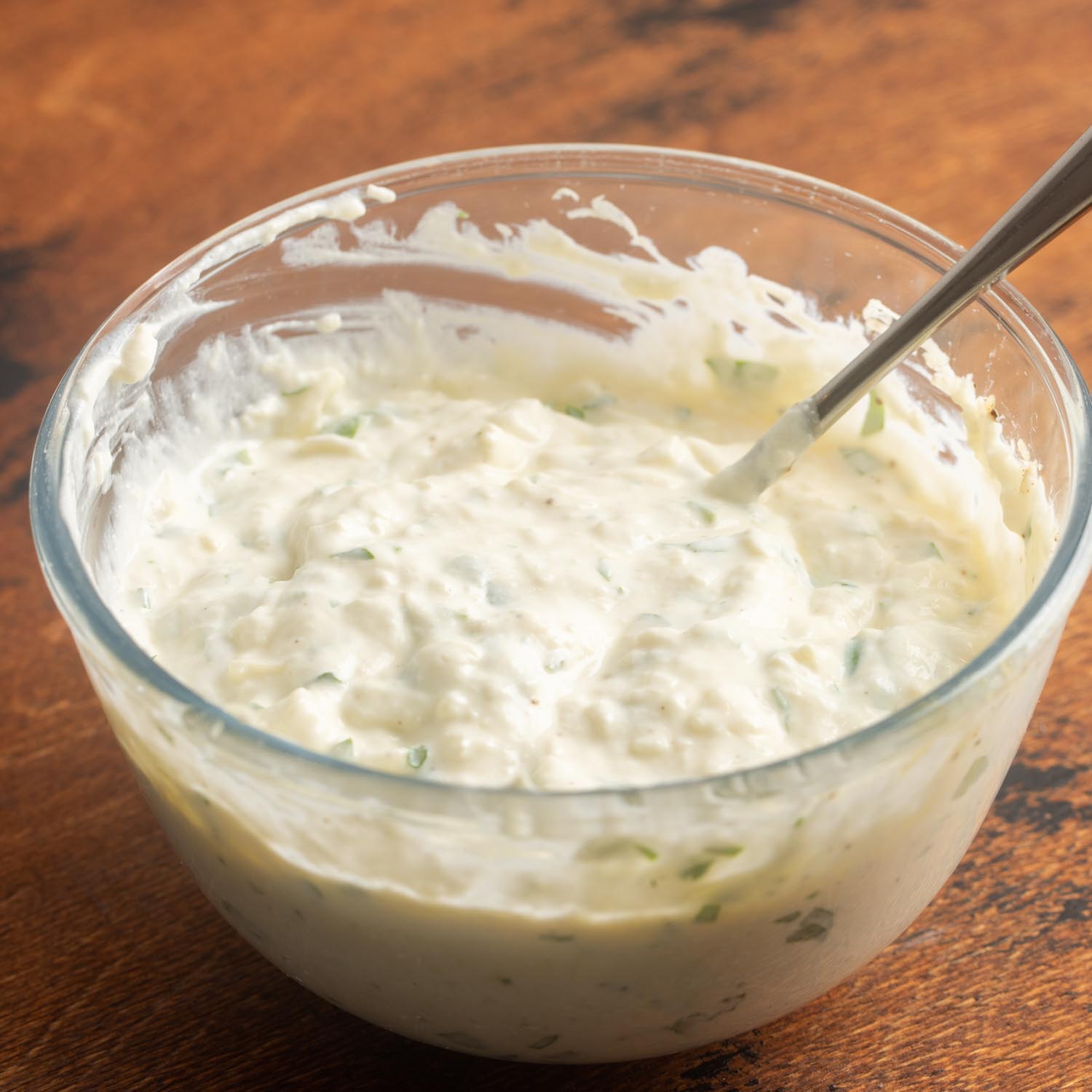 creamy ricotta mixture for lasagna in a glass mixing bowl on a wooden table.