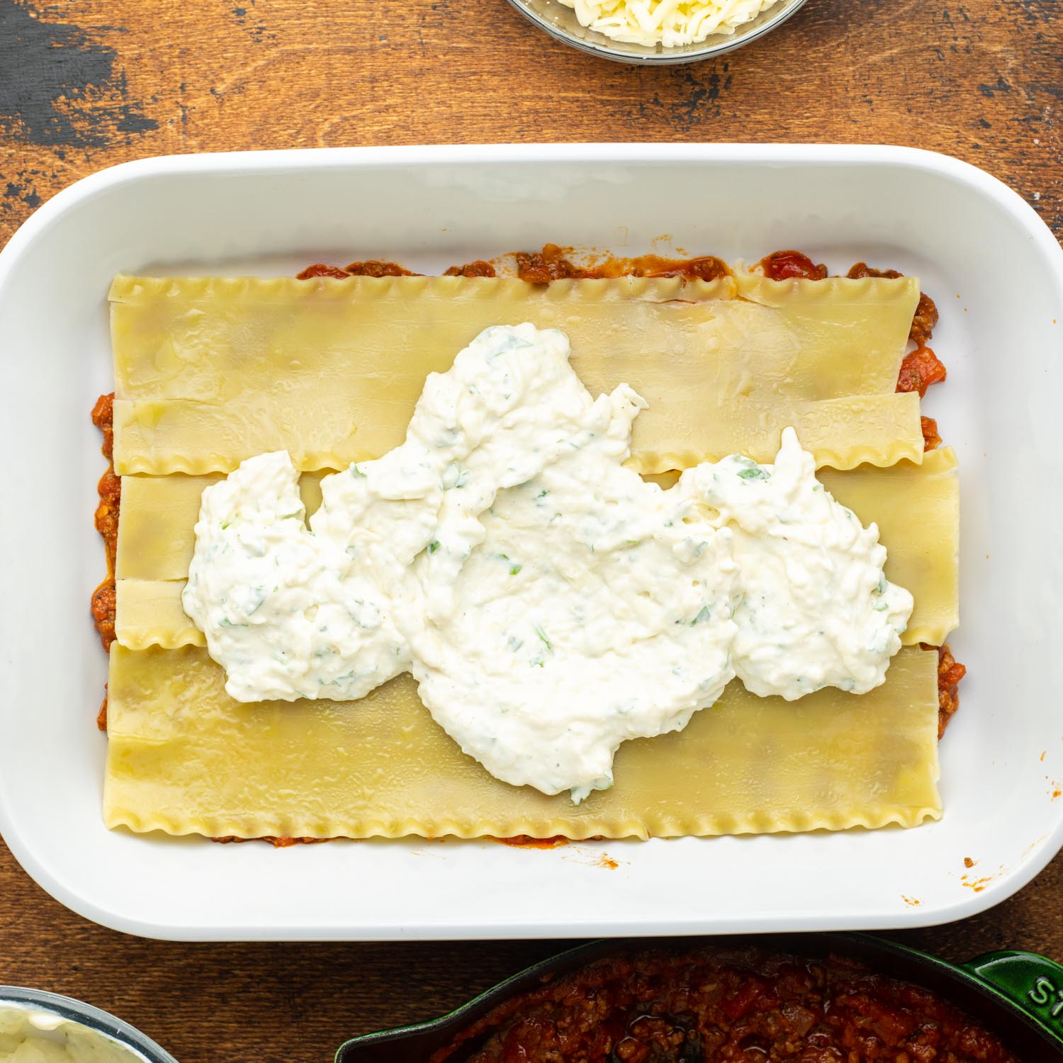 first layers of lasagna in a white casserole dish. Tomato sauce topped with pasta, topped with ricotta cheese.