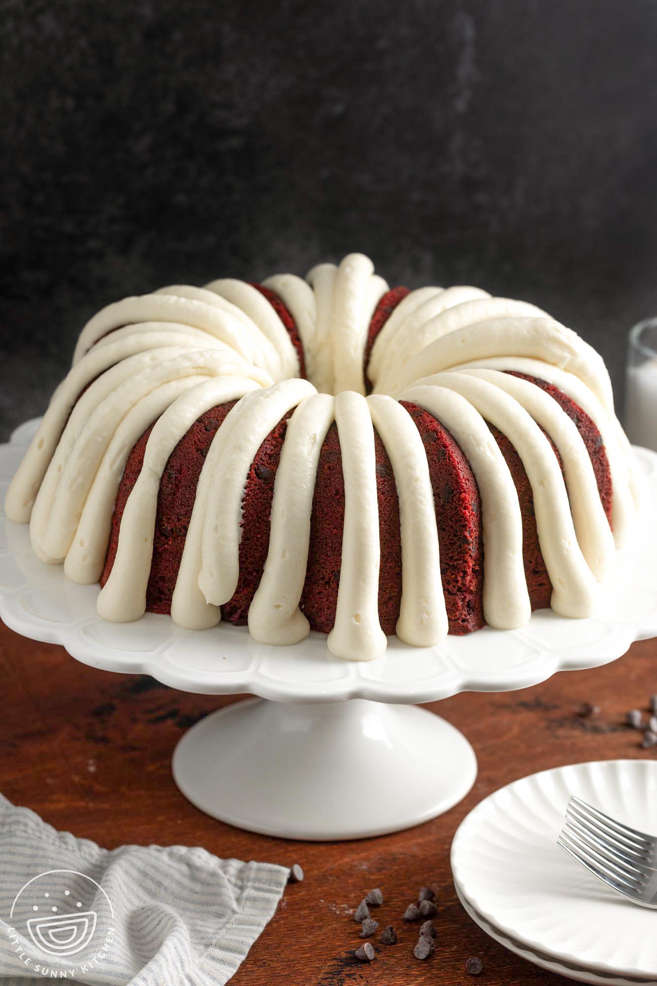 red velvet bundt cake on a cake pedestal topped with thick stripes of frosting.