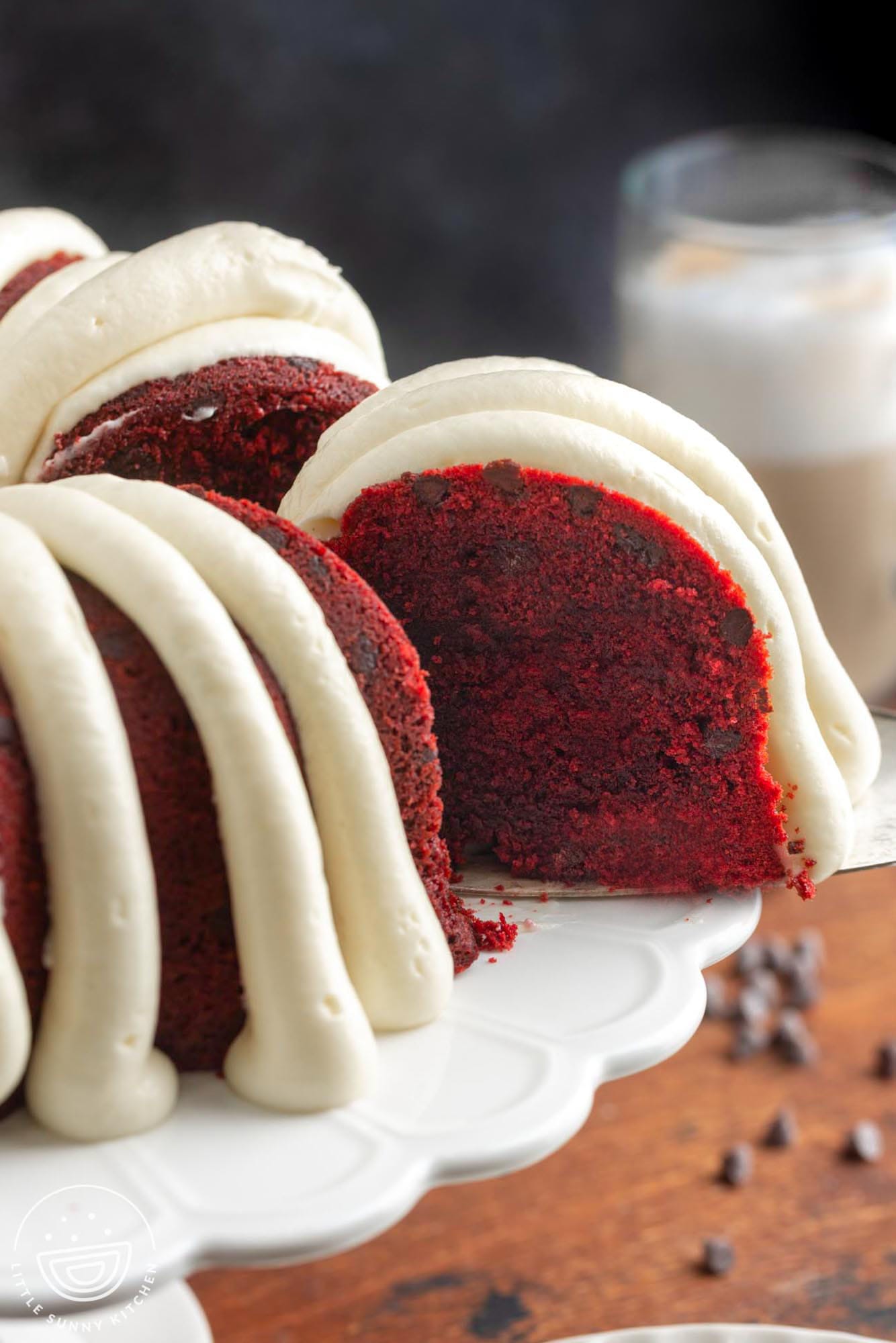 a slice of red velvet bundt cake with chocolate chips and frosting lifted away from the whole cake.