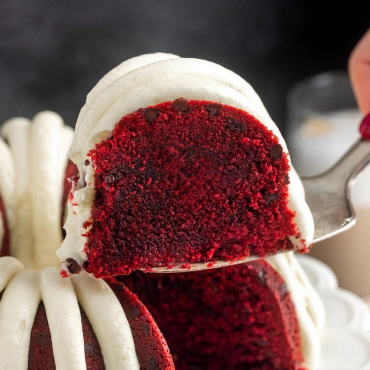 a slice of red velvet bundt cake with chocolate chips and frosting lifted away from the whole cake.