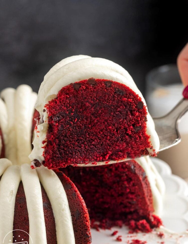 a slice of red velvet bundt cake with chocolate chips and frosting lifted away from the whole cake.