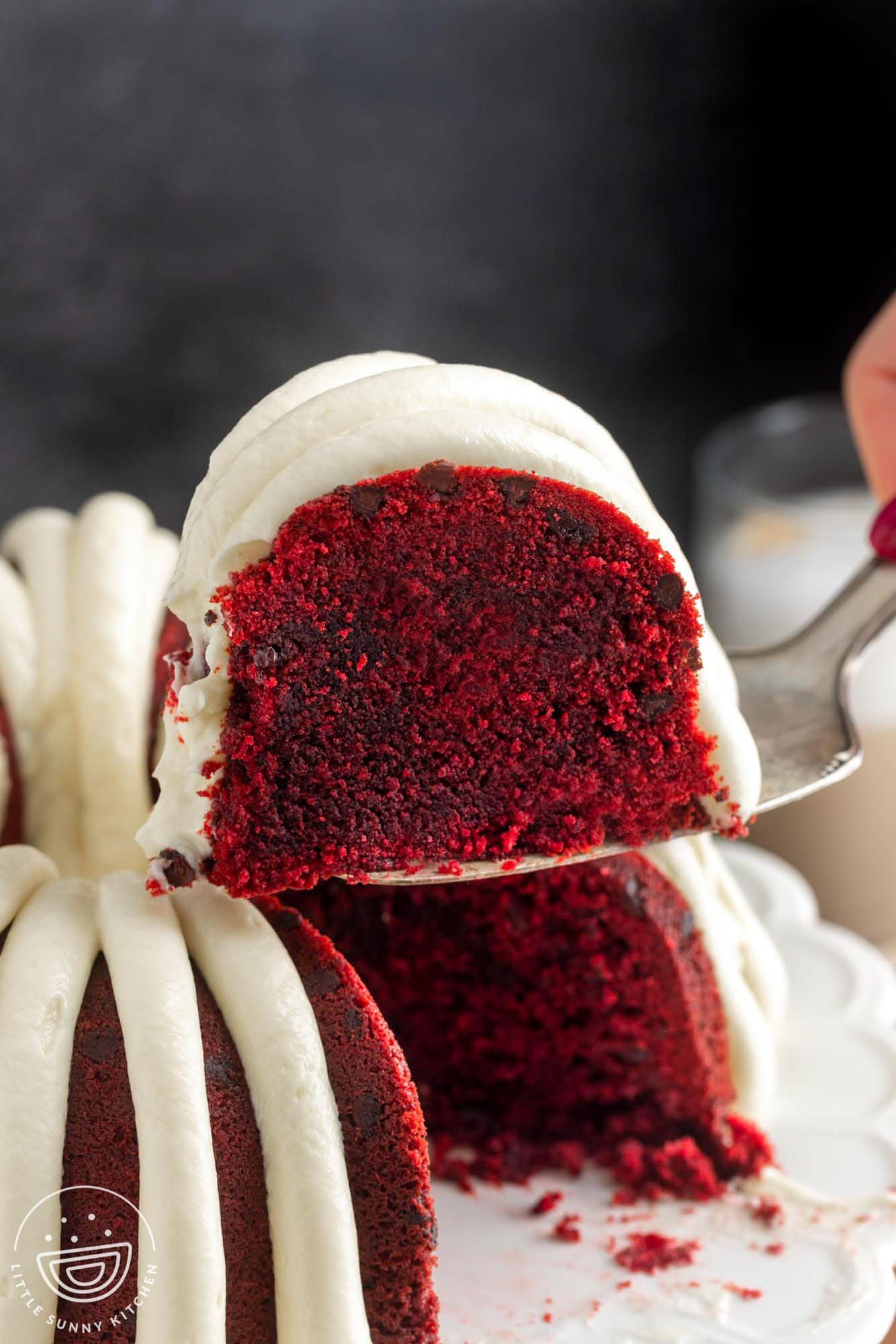 a slice of red velvet bundt cake with chocolate chips and frosting lifted away from the whole cake.