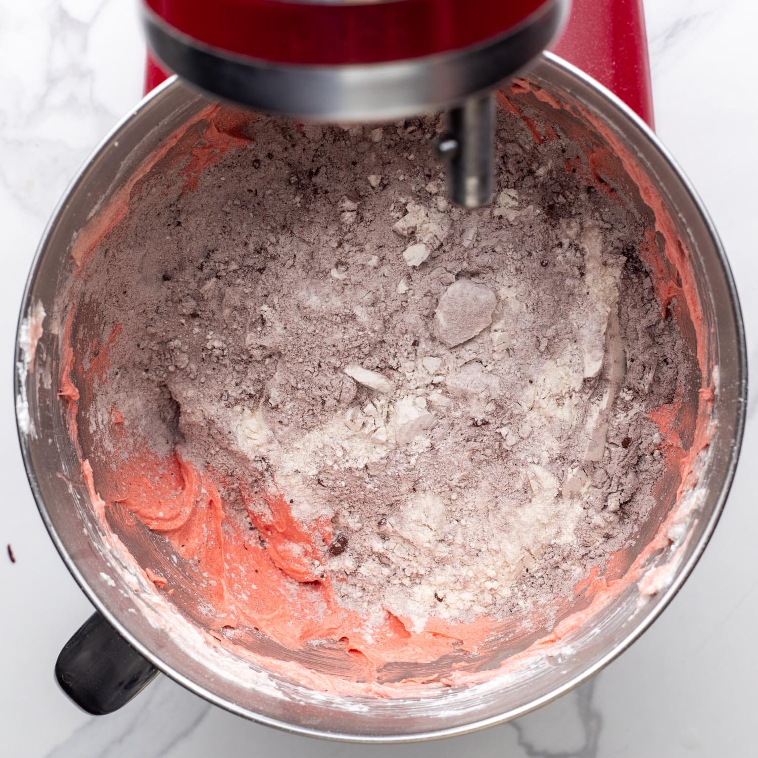 cocoa powder and flour added to red cake batter in a mixing bowl.