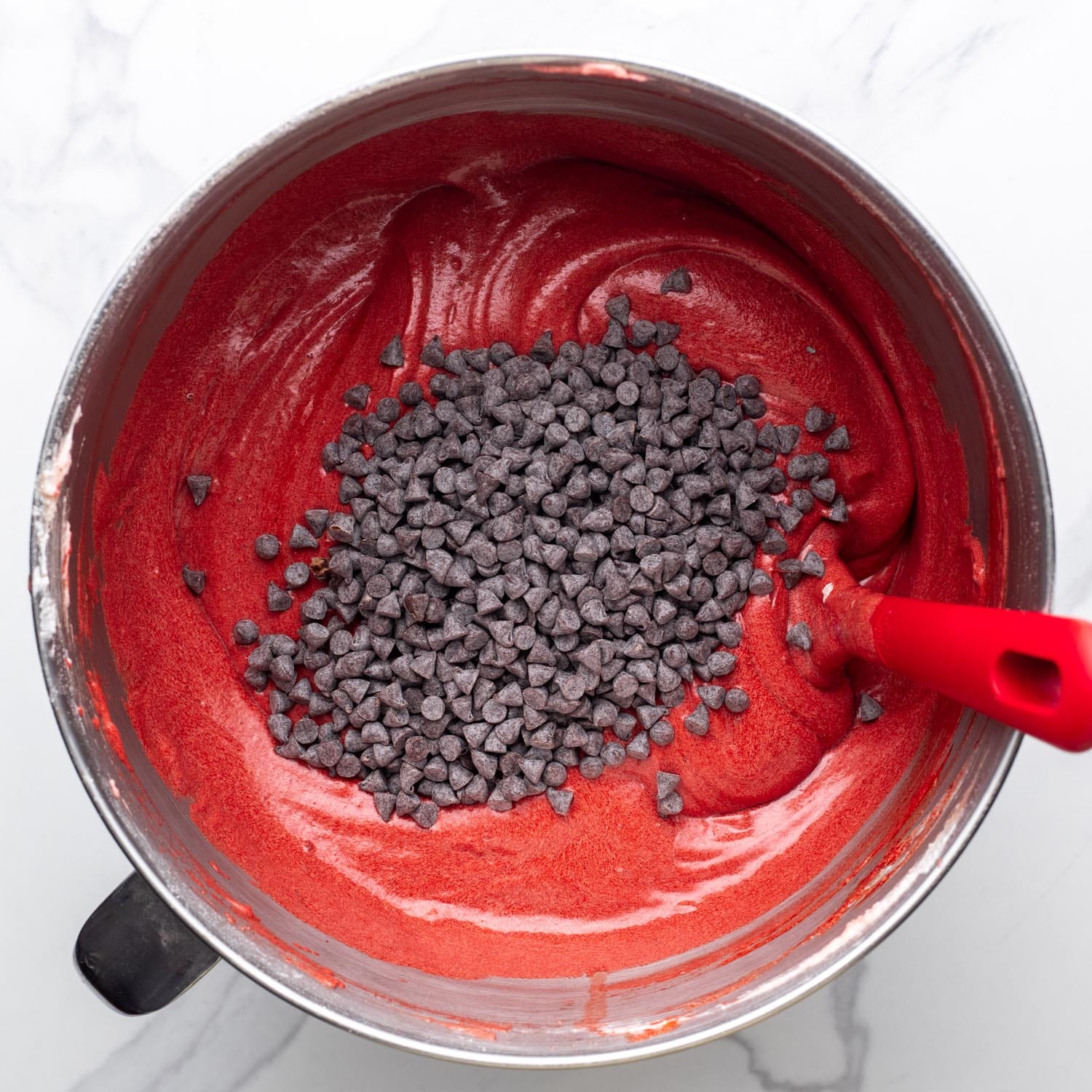 mini chocolate chips added to red velvet cake batter in a mixing bowl.