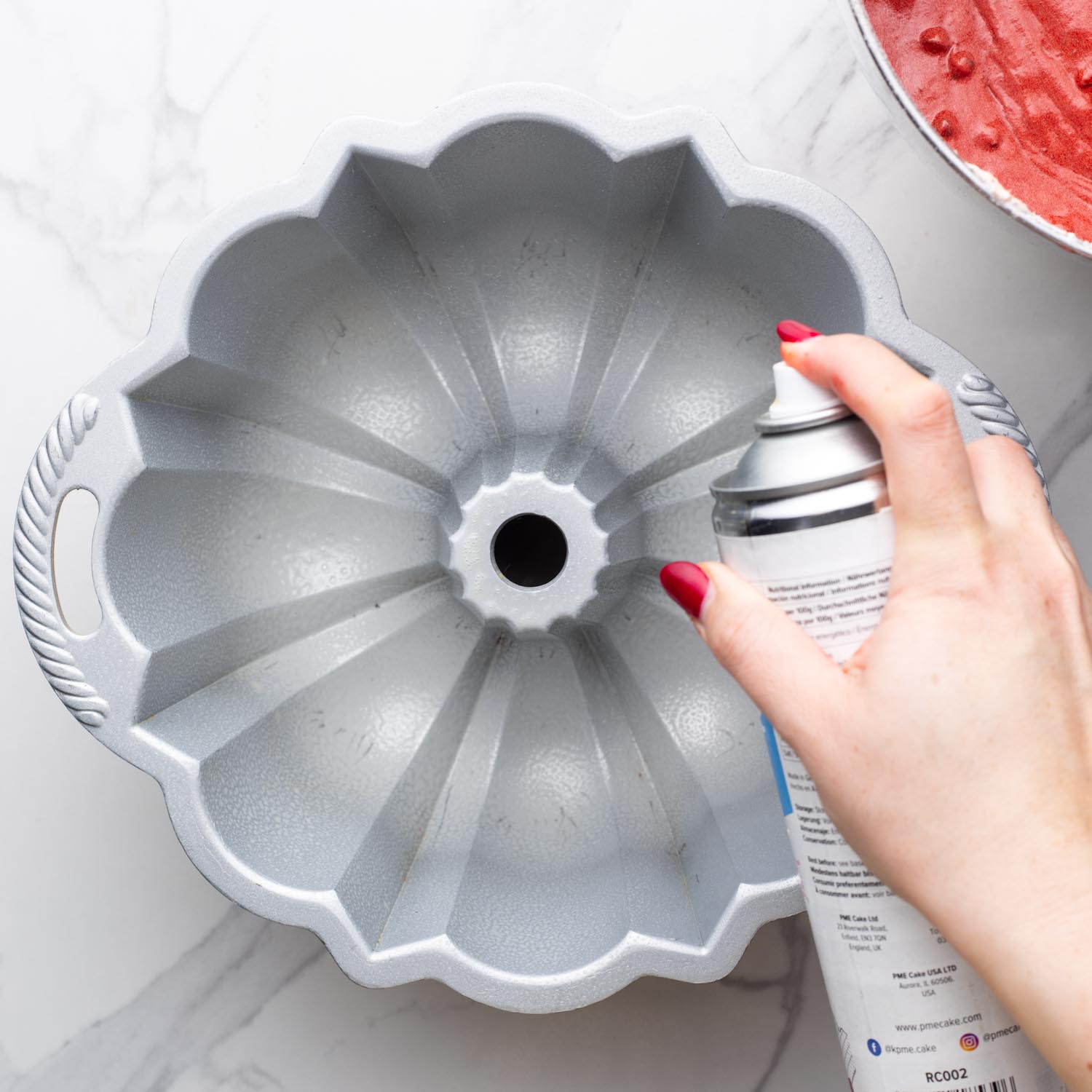 a hand spraying cooking spray into a bundt cake pan.