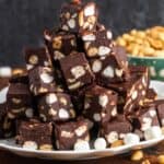 small cubes of rocky road fudge with marshmallows and nuts, stacked on a platter in a pyramid shape.