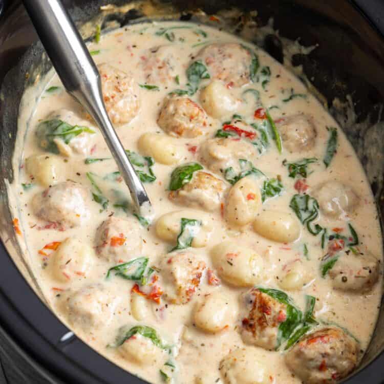 a black slow cooker with tuscan chicken meatballs and gnocchi cooking in it.