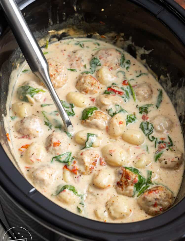 a black slow cooker with tuscan chicken meatballs and gnocchi cooking in it.