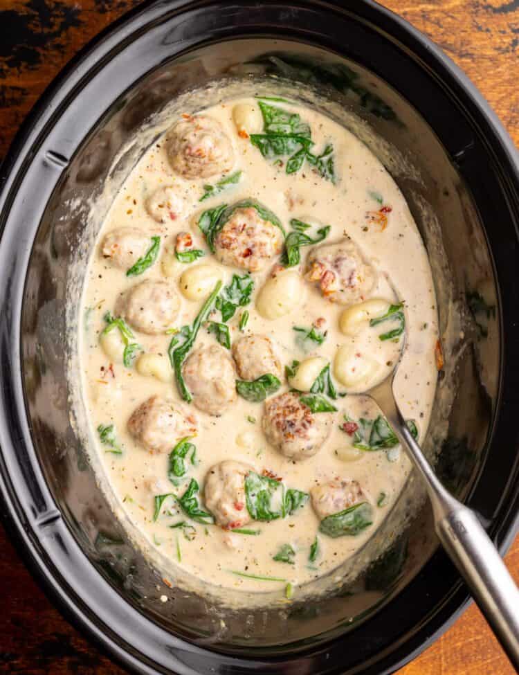 Overhead view of meatballs and gnocchi cooking in a creamy tuscan sauce in an oval crockpot.