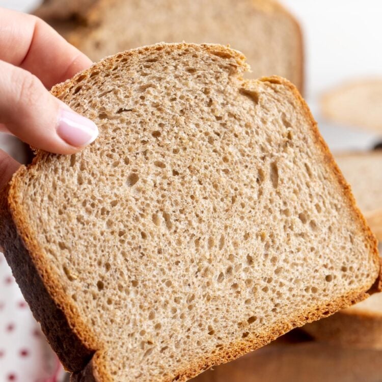 a hand holding up a large slice of soft rye bread that was made in a bread maker.