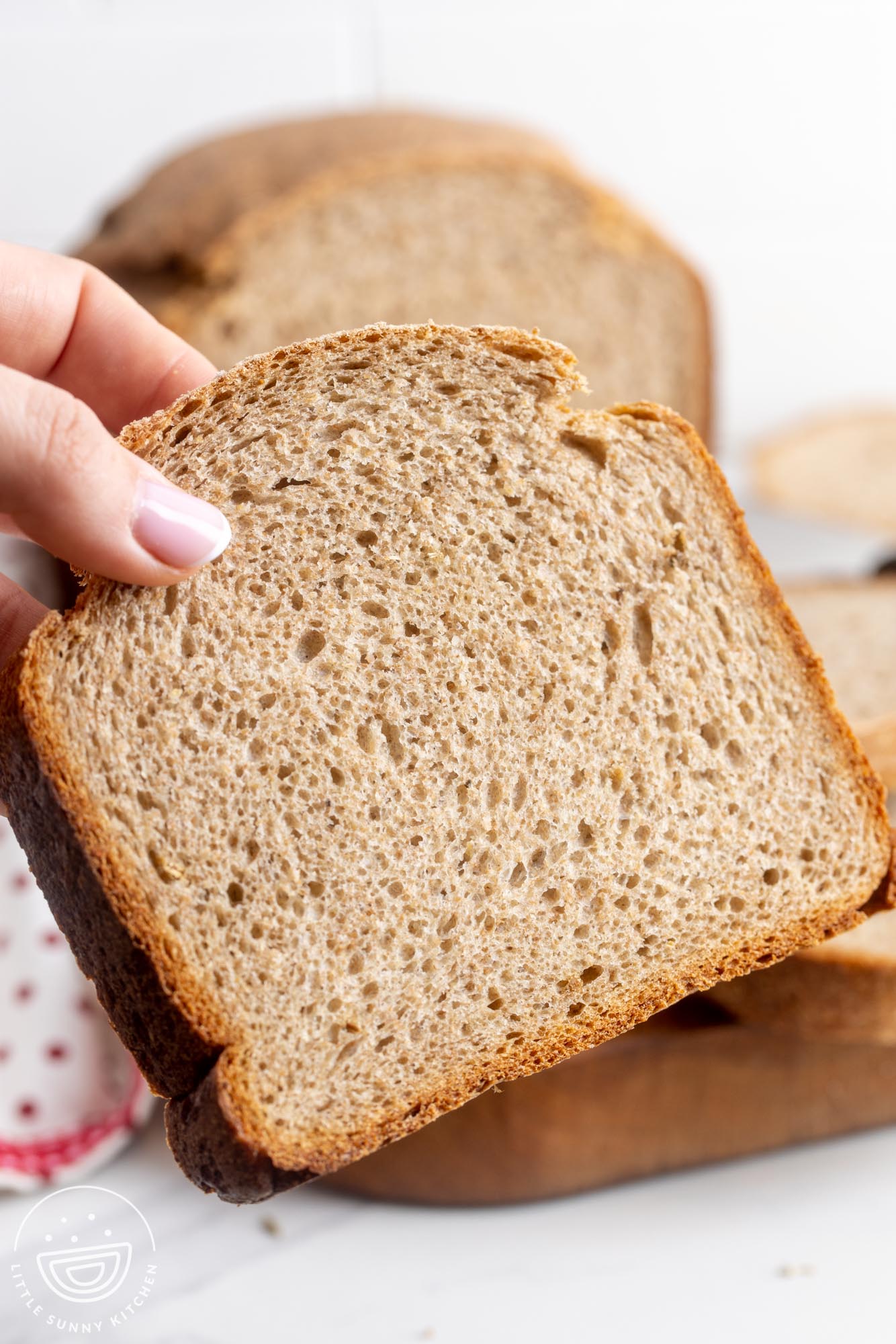 a hand holding up a large slice of soft rye bread that was made in a bread maker.