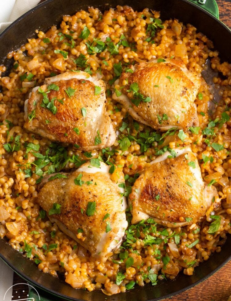 a cast iron skillet of couscous with four chicken thighs on top.