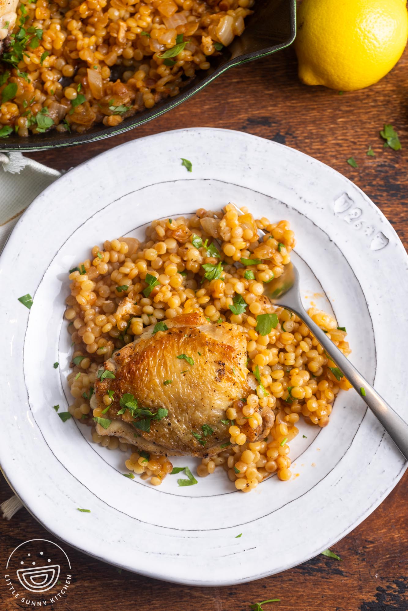 a white ceramic plate of couscous and chicken, with a fork.