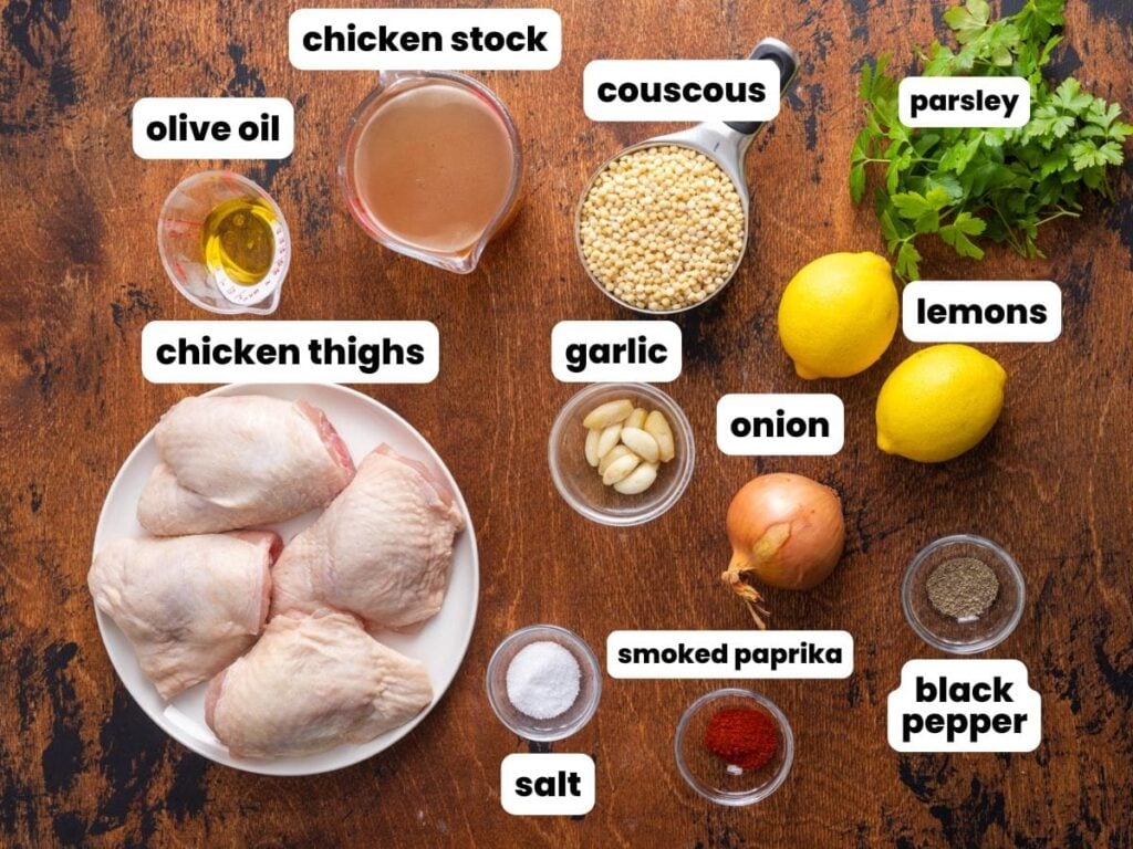 a plate of four bone-in chicken thighs with couscous and seasonings, all in separate small bowls, on a wooden cutting board.