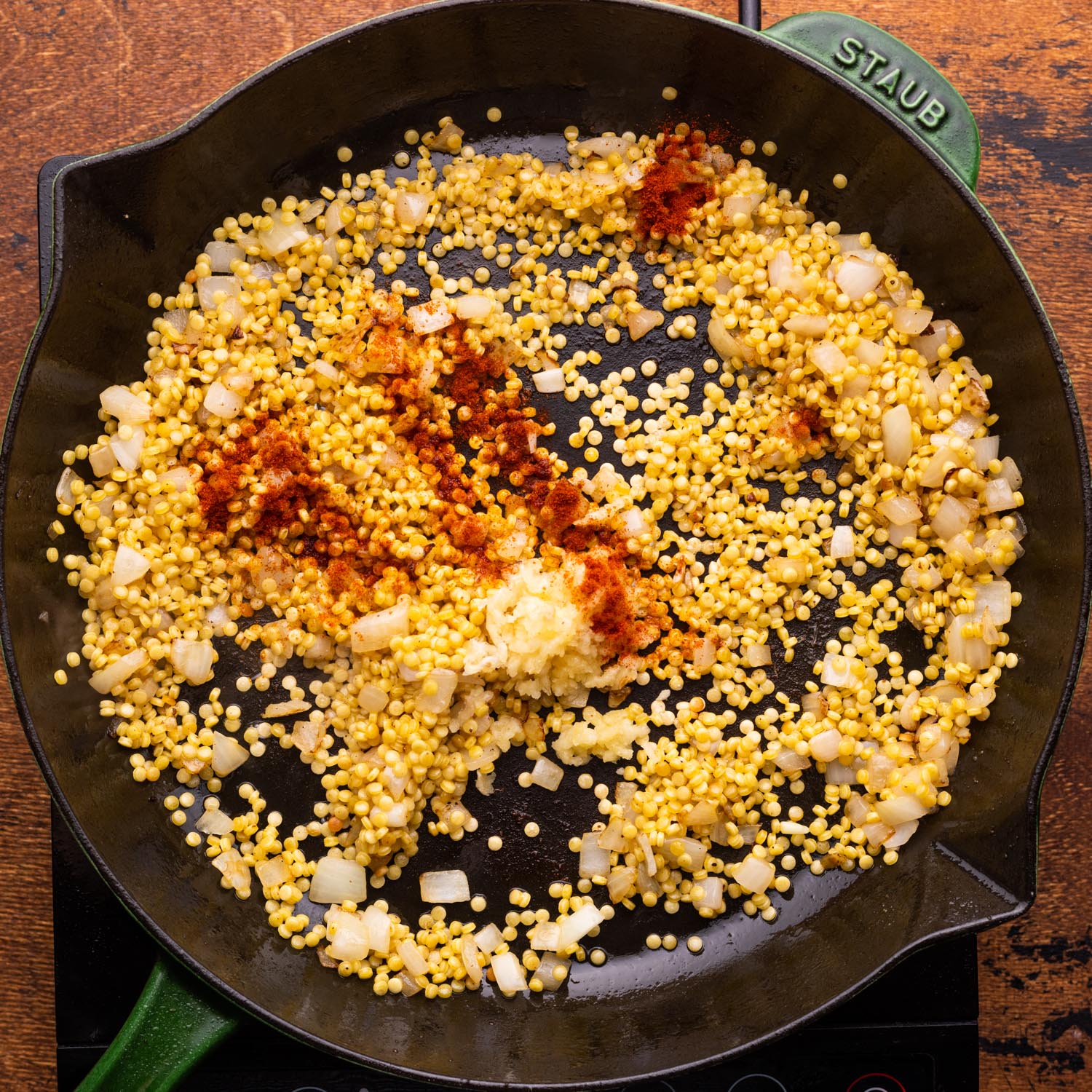 Couscous added to a skillet along with seasonings.