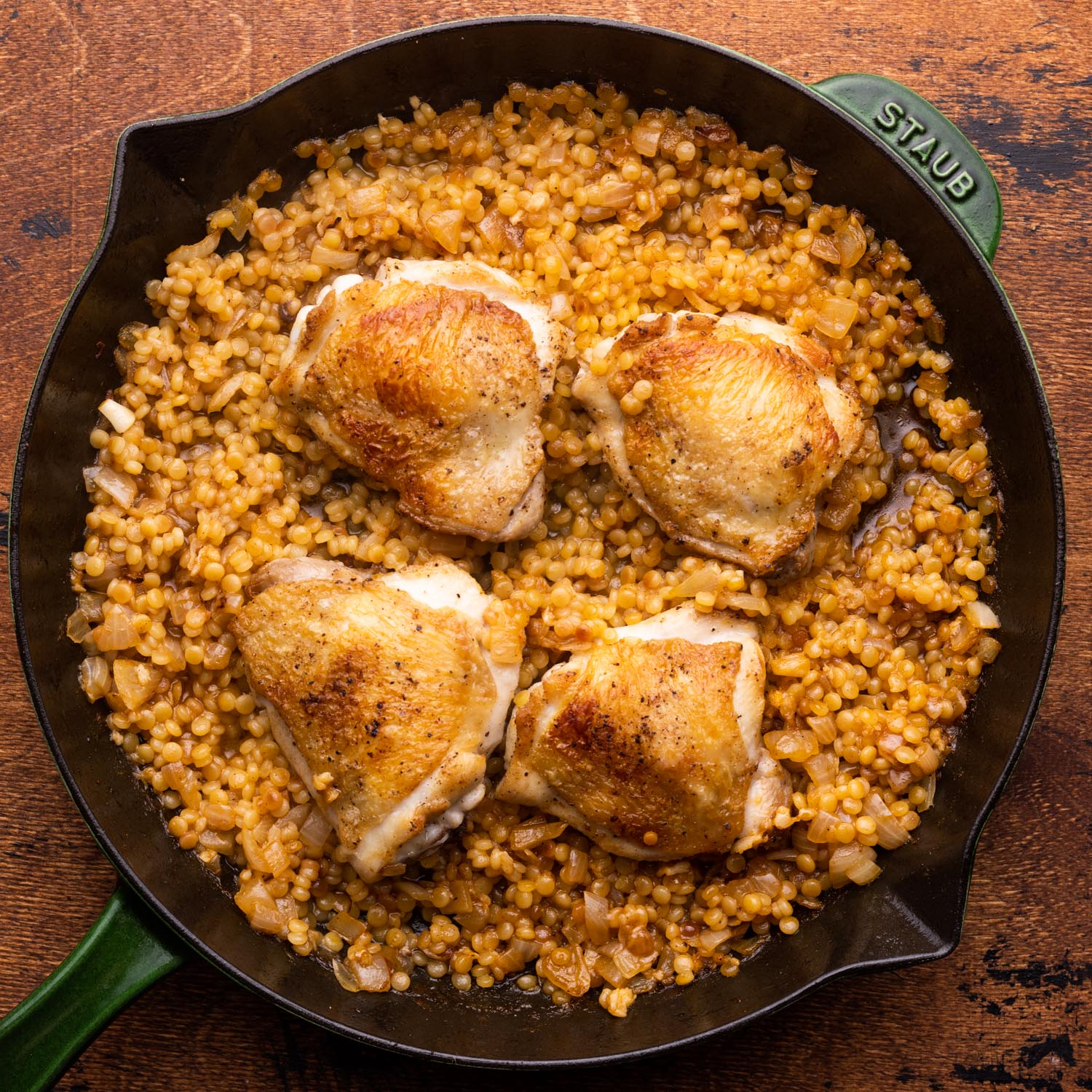 chicken thighs and couscous in a cast iron skillet.