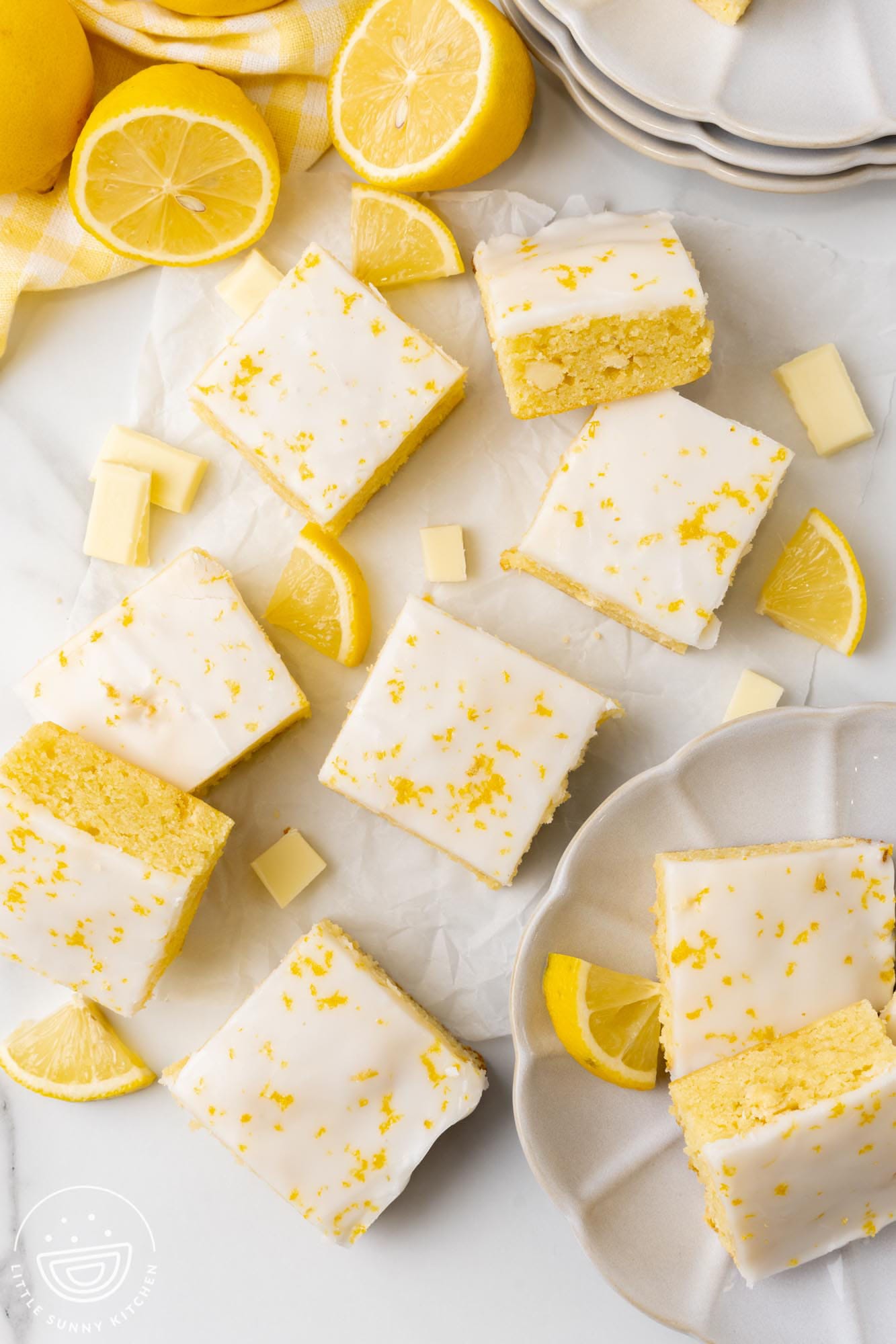 Lemon brownie squares spread on parchment paper. Fresh lemon wedges and white chocolate chunks are spread around them.