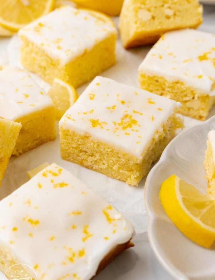 Closeup of chewy lemon brownie squares with white icing and lemon zest on top.