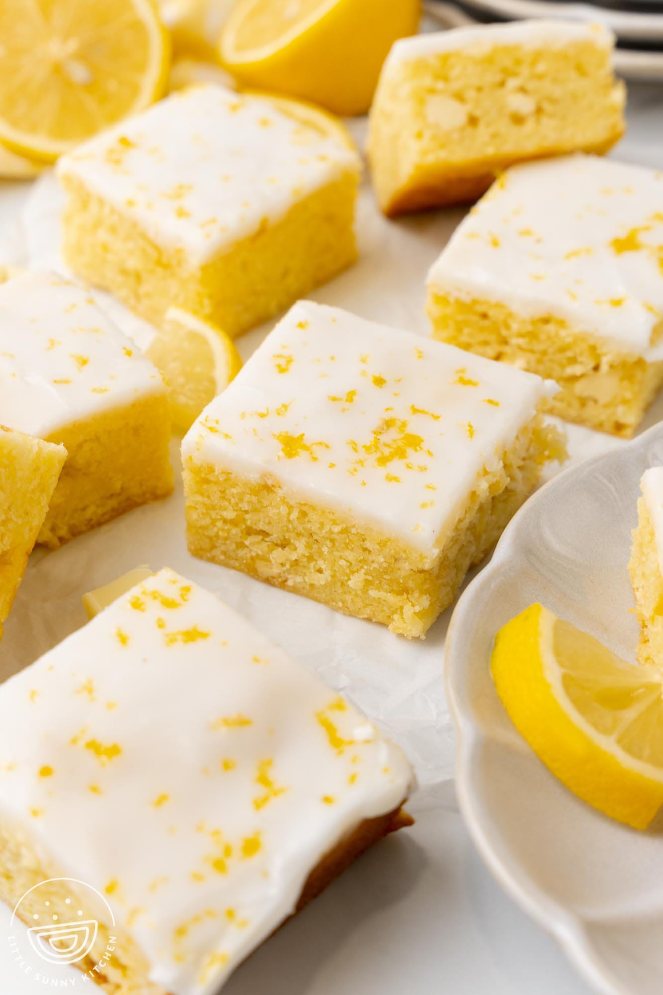 Closeup of chewy lemon brownie squares with white icing and lemon zest on top.