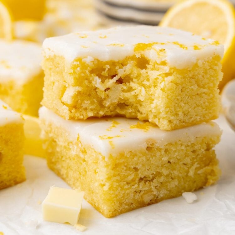 a stack of two iced lemon brownies. The top one has a bite taken to show the dense, chewy texture.