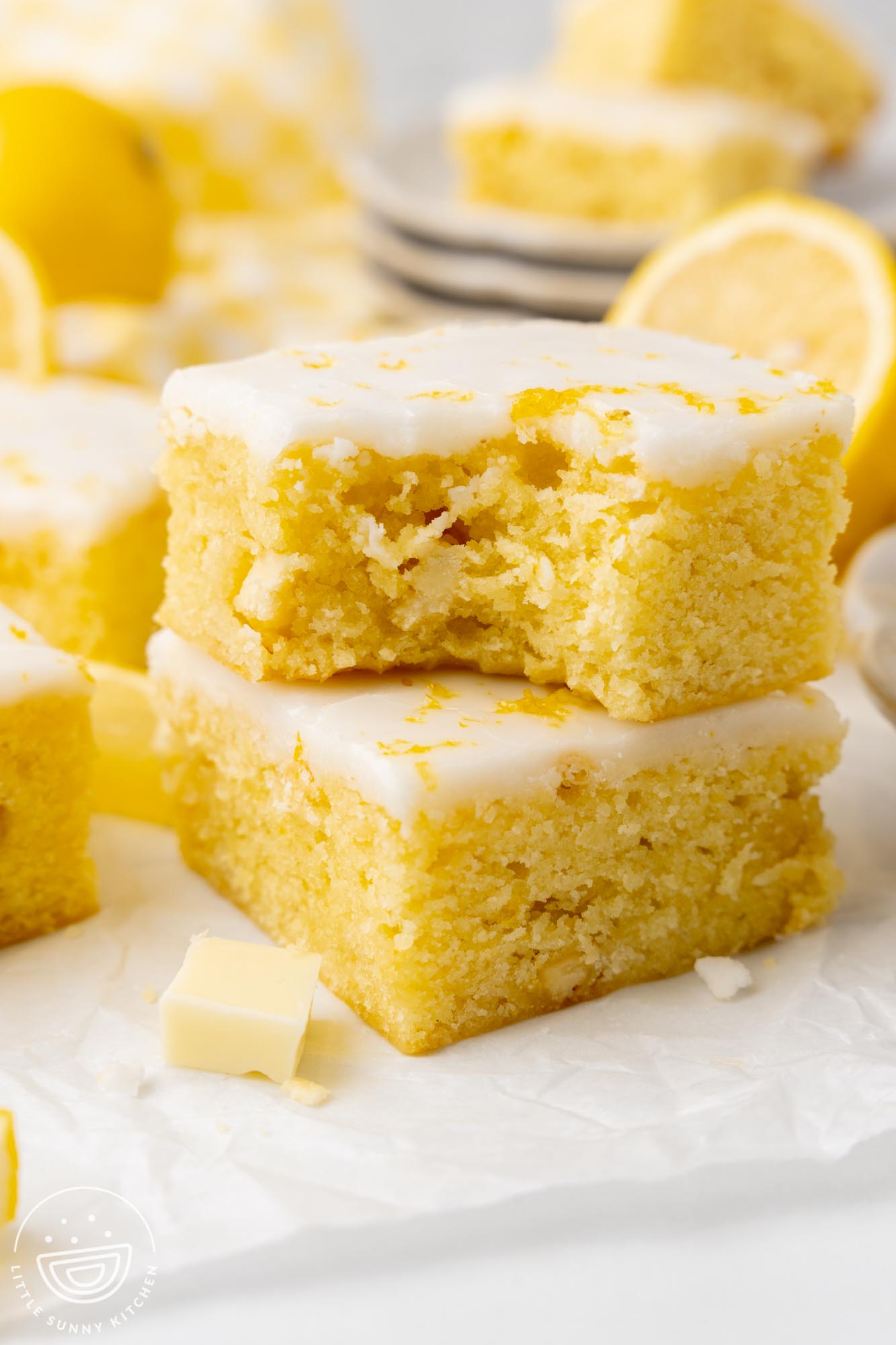 a stack of two iced lemon brownies. The top one has a bite taken to show the dense, chewy texture.