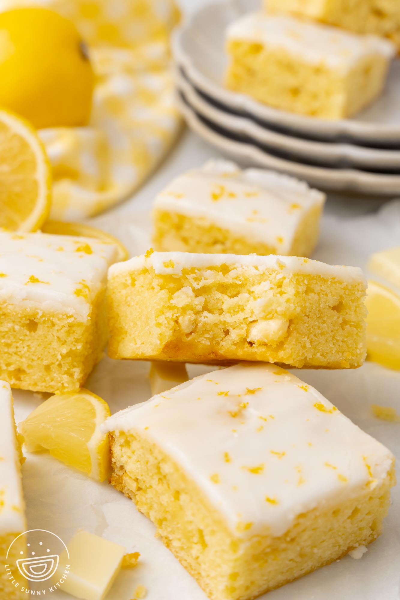 Lemon brownies on a white surface. One has had a bite taken to show the chocolate chunks inside.