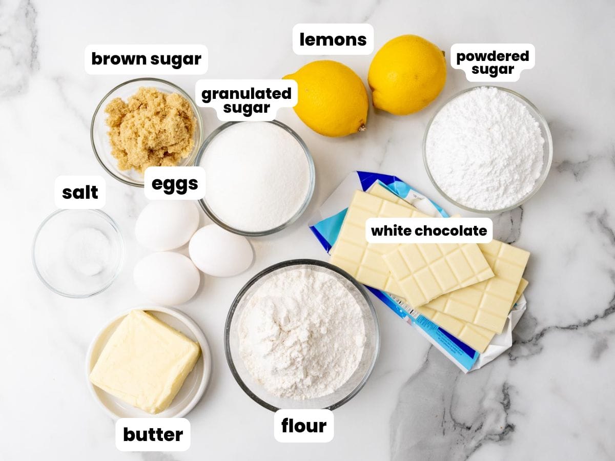 Ingredients for Lemon Brownies with white chocolate, all in small bowls, arranged on a marble counter.