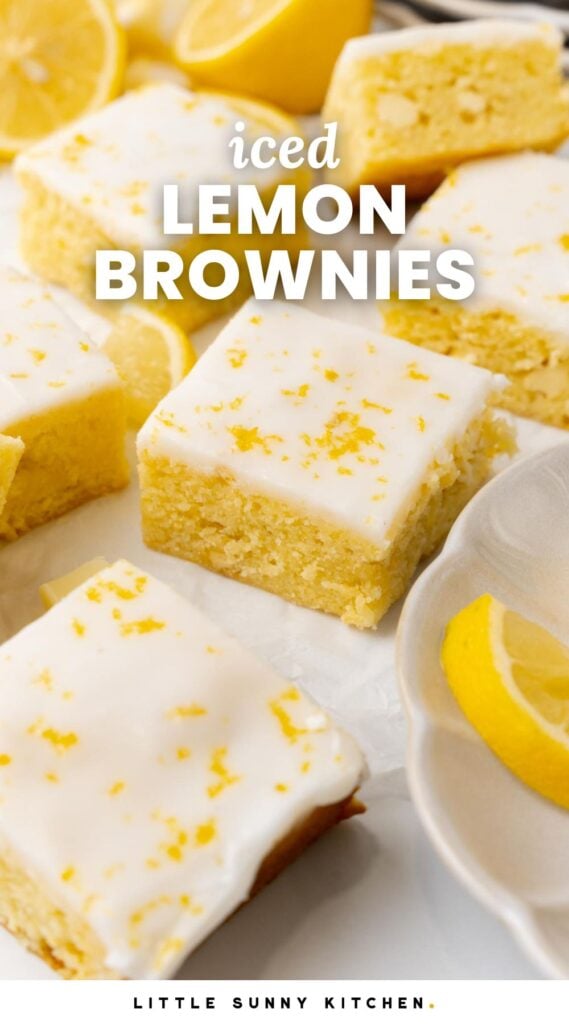 Lemon brownie squares with white icing on a white surface. Fresh cut lemons are in the background. Text overlay says "iced lemon brownies"