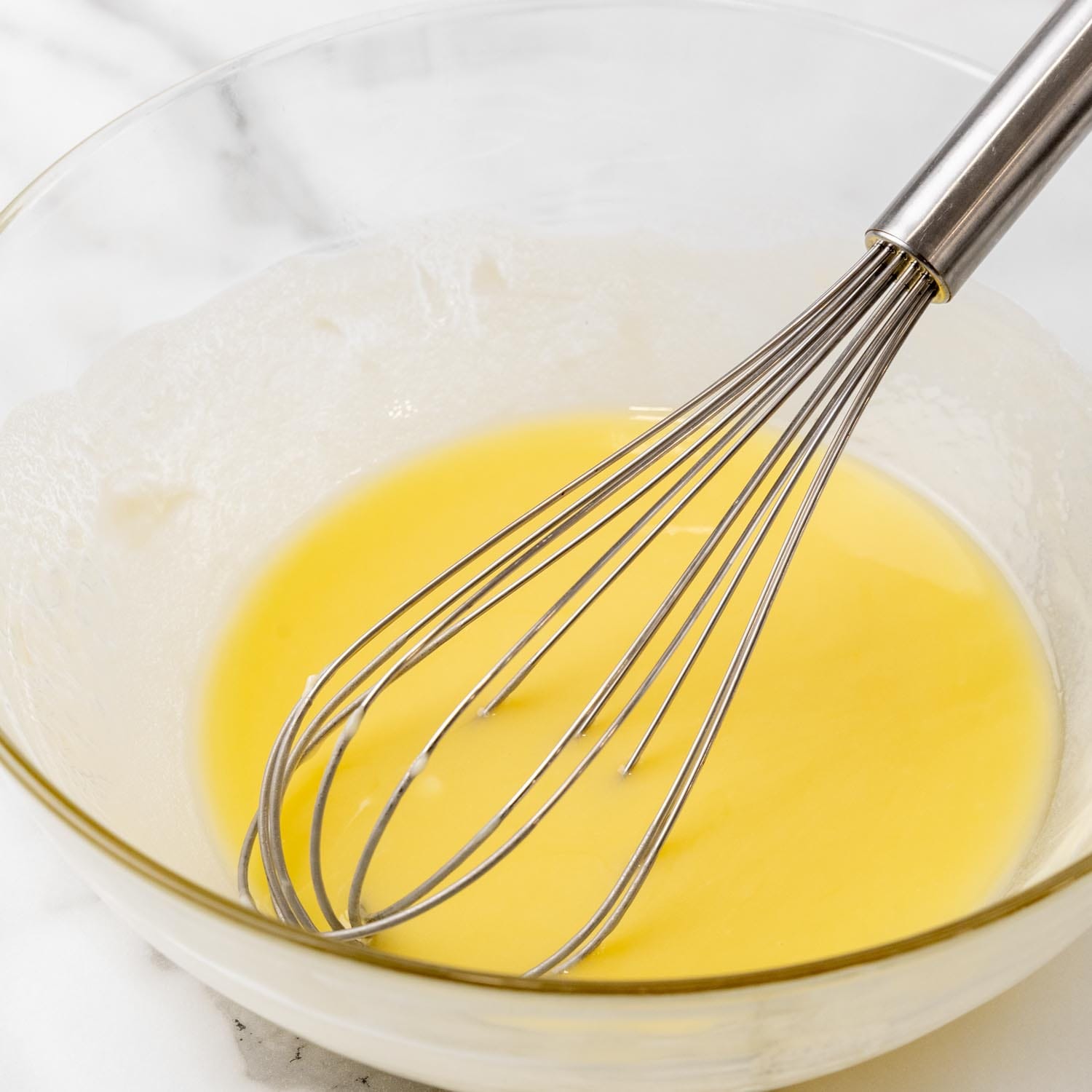 A glass bowl of melted butter with white chocolate, stirred with a whisk.