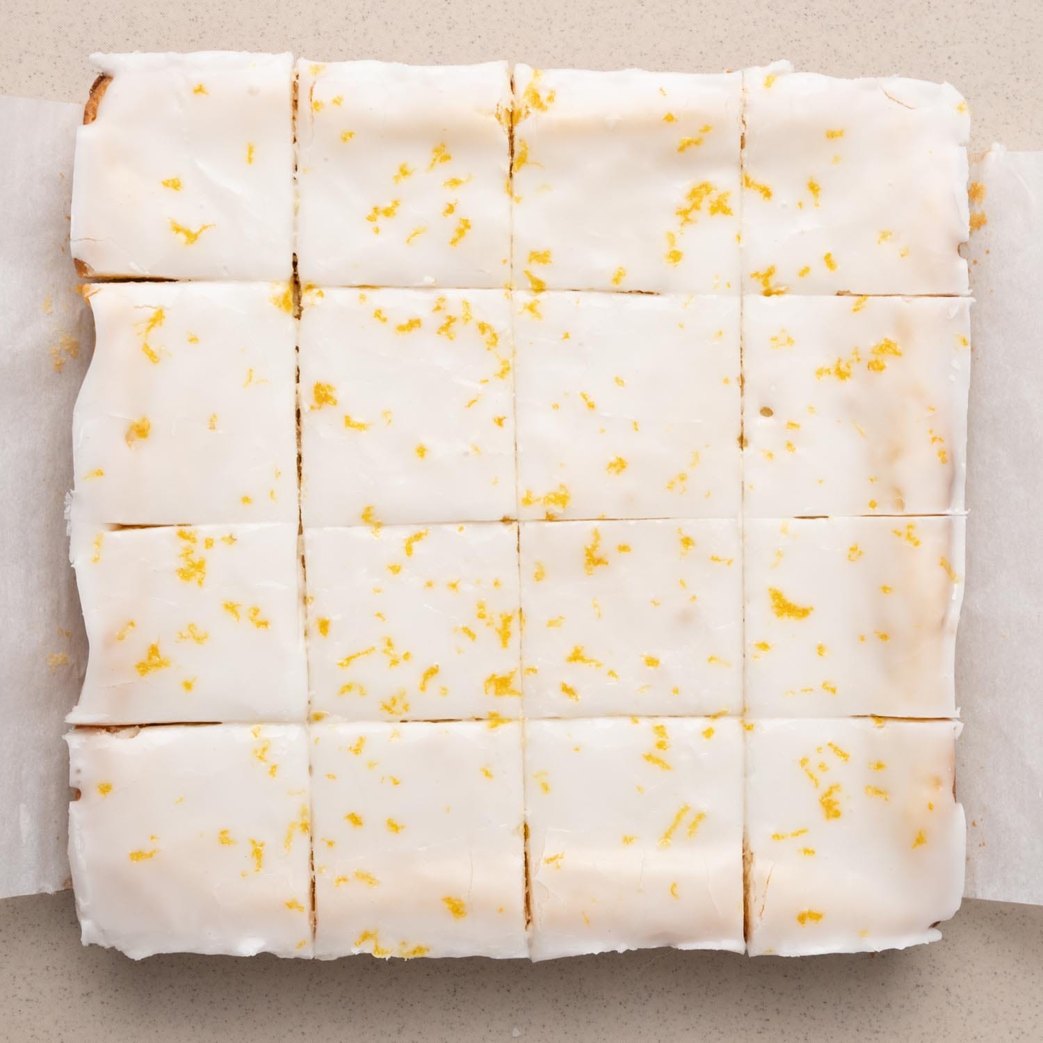 Lemon brownies, removed from the pan and cut into 16 squares. The icing is sprinkled with lemon zest.