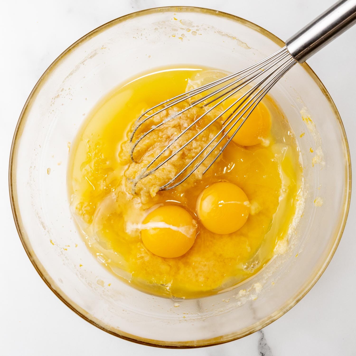 Eggs and lemon juice whisked into a lemon brownie batter in a bowl, viewed from overhead.